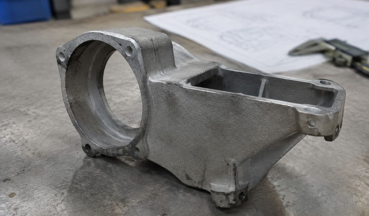 Representative cast housing beside a technical drawing and caliper.