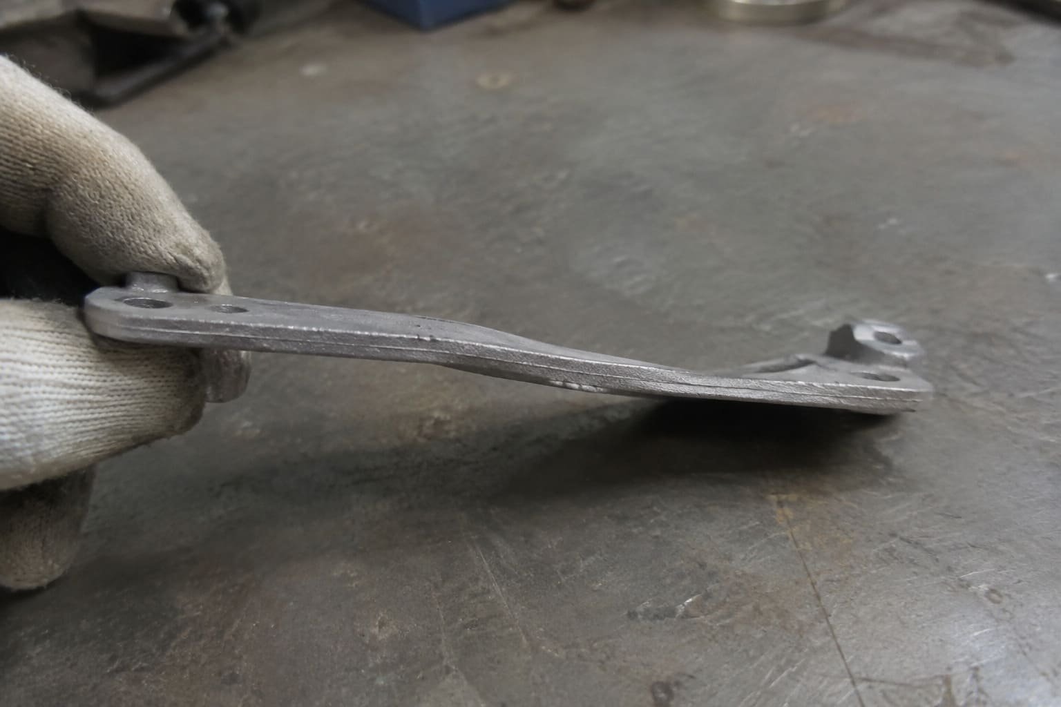 Gloved hand supporting a long thin cast bracket with visible curvature.