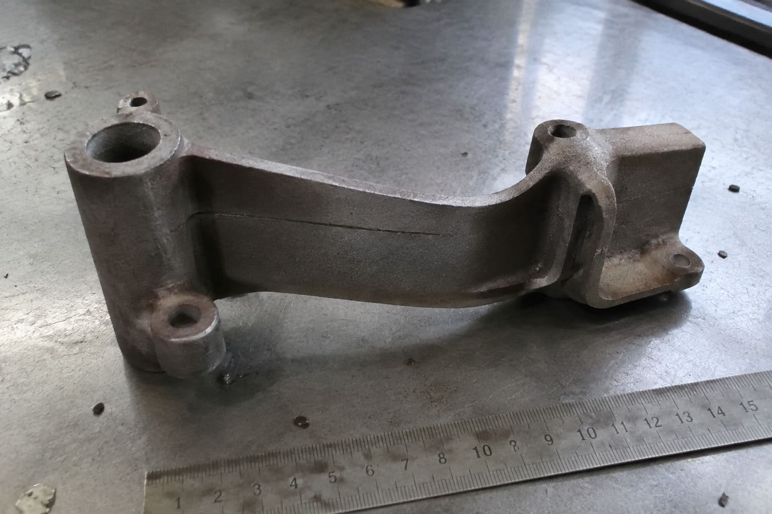 Thin-wall cast bracket positioned beside a ruler for geometry review.