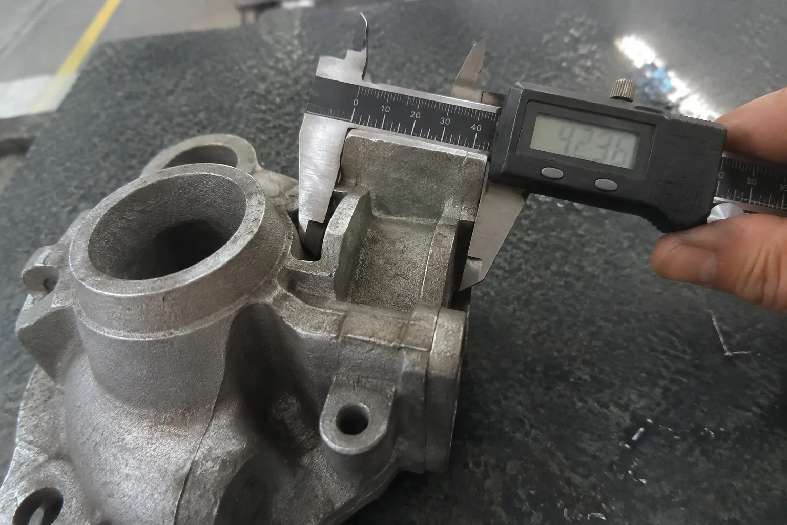 Inspector using a caliper to measure a complex investment cast part on a granite surface plate